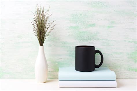 Download Black coffee mug mockup with dark meadow grass in vase and books.